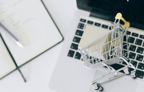 Creative depiction of online shopping with a miniature cart on a laptop keyboard.
