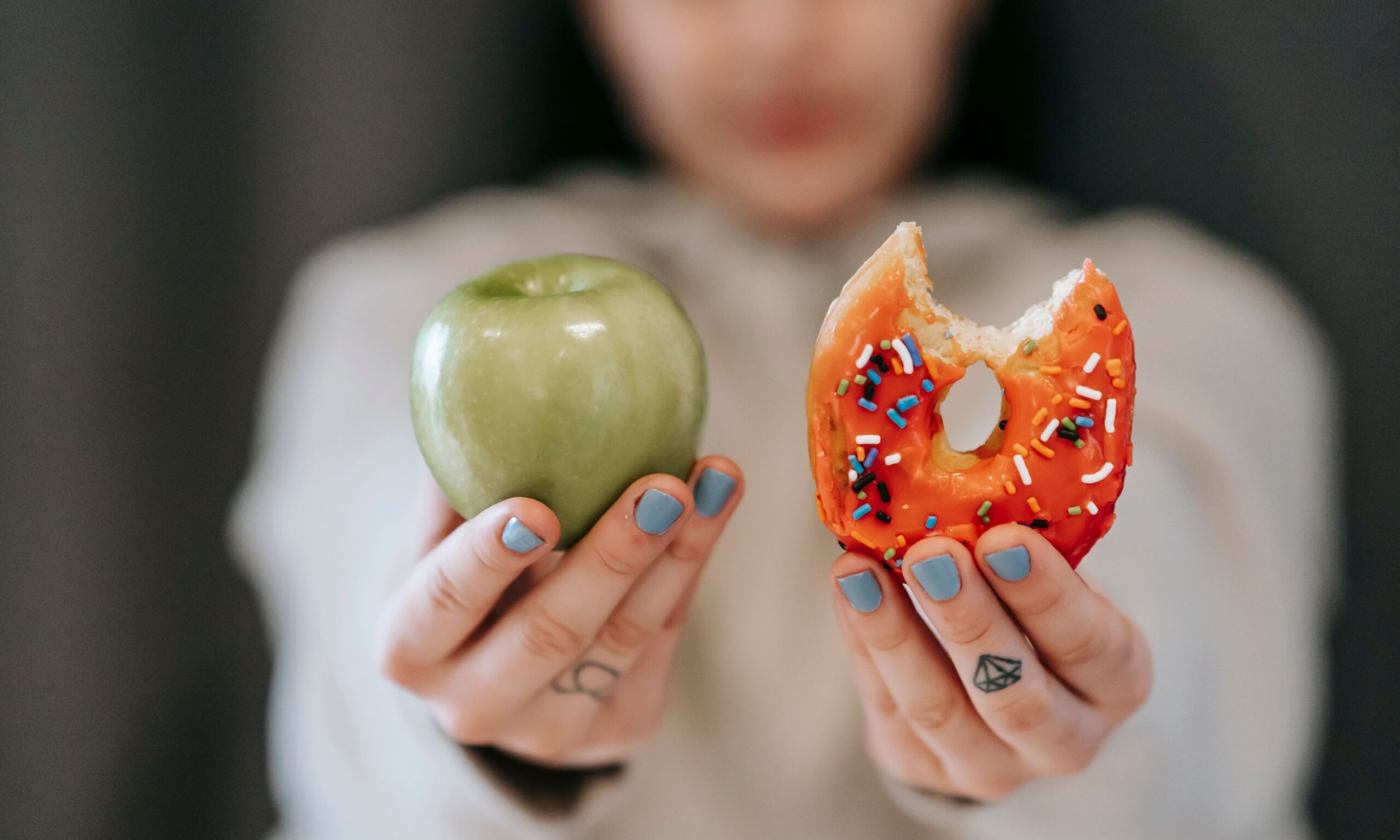 female demonstrating delicious sweet donut and fresh green apple while making decision