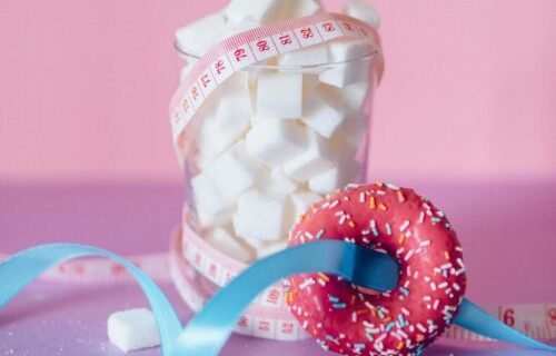 Vibrant image highlighting sugar awareness using a donut and tape measure on pink backdrop.